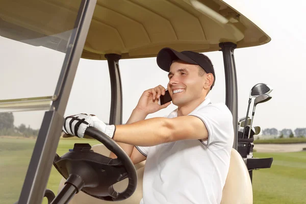男人坐在一辆高尔夫球车和谈电话 — 图库照片