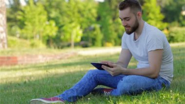 Çimenlerin üzerinde oturan ve tablet bilgisayar kullanarak bir çocuk