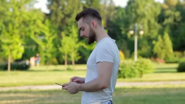 Joven parado en el parque con una tableta — Vídeos de Stock