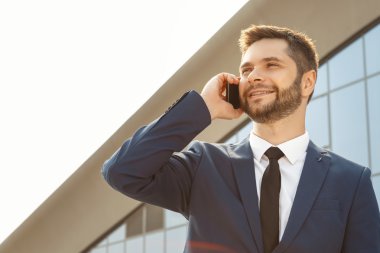 Genç işadamı dışarıda telefonla konuşuyor.