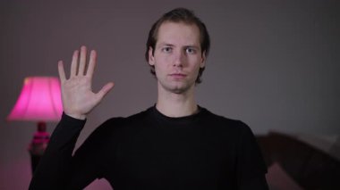 Beyaz adam içeride elleri ile sayarak siyah gömlek nötr yüz arkaplan yakın oturan pembe arka plan oturma odası ardışık çerçeveler sunucu giriş gösterir,