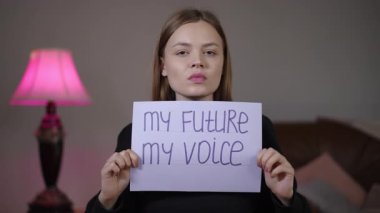 Geleceğimi tutan genç beyaz kadın yatak odamda imzam pembe lambanın yanında el yazısıyla yazılmış mor harfler aktivist gençlik lideri kişiliği kendinden emin konuşmacı enerjisi kampanya görüntüleri.
