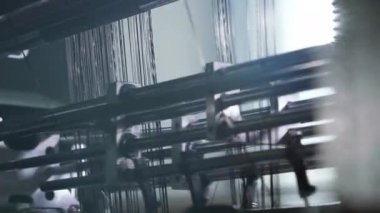 Dinamik kamera hareketi dokuma makinesinin metal çerçevesinde kayan iplikleri ortaya çıkarırken yumuşak anamorfik alevler ve kayan ışık endüstriyel tekstil çalışmalarını vurguluyor