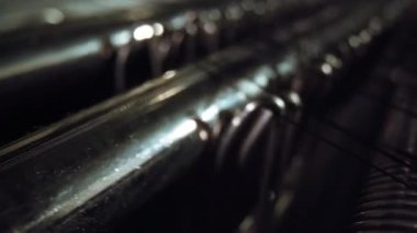 Yakın makro çekim, yumuşak röfle yakalayan parlak metal çubukları gösteriyor. Bu arada ince tekstil iplikleri, sığ odaklı, dengesiz bir endüstriyel atmosfer yaratıyor.