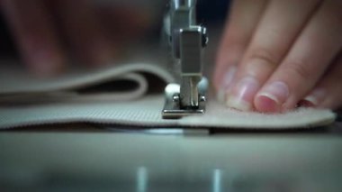 Katmanlı kumaş dikiş makinesinin ayağının altına yönlendirilir parmak uçları kenarı sabit tutarken, yumuşak sinematik bokeh dikiş çizgisi etrafında sakin odaklı bir atmosfer yaratır.