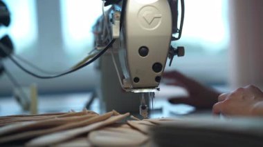 Dikiş makinesi iğnesinin altındaki bej kumaş katmanları, gün ışığını, pürüzsüz dokuları ve tekstil üretim sürecinde odaklanmış iş akışını gösteriyor.