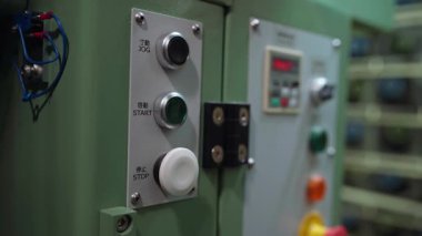 Bir el, endüstriyel kontrol panelindeki yeşil başlatma düğmesine sıkıca basarak, hassas işlemleri, metal devreleri, temiz etiketleri ve tekstil üretim ortamındaki odaklı iş akışını gösterir