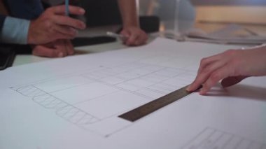 Eller bir mimari düzeni incelerken bir cetvel ve kalem tutar, odaklanmış bir işbirliği planlama oturumunda düz çizgiler ve yapısal bölümleri inceler