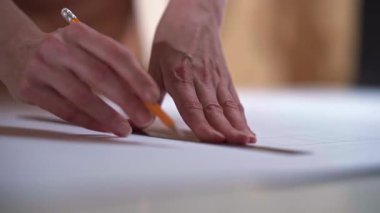 Eller beyaz çizim yüzeyinde bir kalemle temiz desenler çizer, düzenli hareketler ve odaklanmış dikkat ile tekstil işleri için doğru şekiller yaratır.