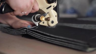 Yakından bakıldığında, yoğun teknik kumaşın çoklu istiflenmiş katmanlarını kesen bir elektrik roter kesicisini gösterirken, kılavuz bir el malzemeyi sabit ve hizalı tutar.