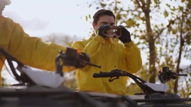 Beyaz sürücü sarı ceketli gözlükleri ayarlar, sonbahar ağaçlarının altındaki dörtlü gidonu kavrayıp, odaklanmış ifadeyle off road yolculuğuna hazırlanır ve katmanlıdır.