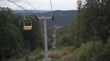 Dağ vadisine inen bir kayak asansörünün kişisel perspektifi. Yöneticiler sık yeşil orman manzarasının üzerinde bir aşağı bir yukarı hareket ederler.