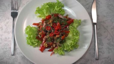 Et, fasulye, ceviz ve kırmızı biberli taze, baharatlı bir Gürcü salatasının beyaz bir tabakta yavaşça dönüşümü.