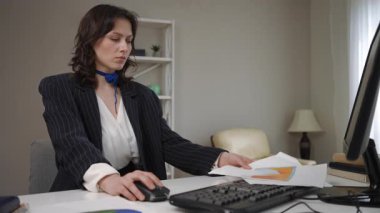 Genç bayan çalışan masasında oturuyor, işine konsantre oluyor. Fare 'ye tıklıyor ve klavyede yazıyor.