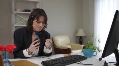 Evde uzaktan çalışırken arızalı ya da bozuk bir bilgisayar faresiyle boğuşan, kulaklıklı genç bir iş kadını.