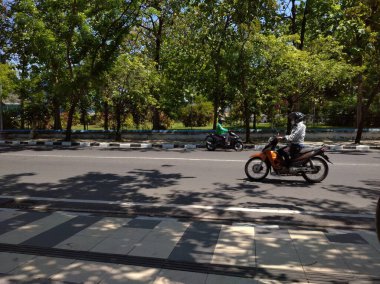 Semarang, Endonezya, 4 Temmuz 2021 - Arabası, motosikleti ve yemyeşil ağaçları olan bir şehir caddesi