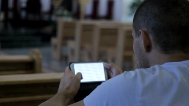 Молодой человек читает Библию по телефону в церкви — стоковое видео
