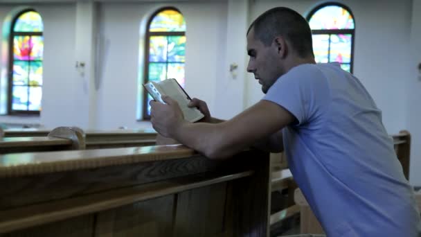 Молодой человек, читающий Библию в церкви — стоковое видео