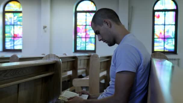 Молодой человек, читающий Библию в церкви — стоковое видео