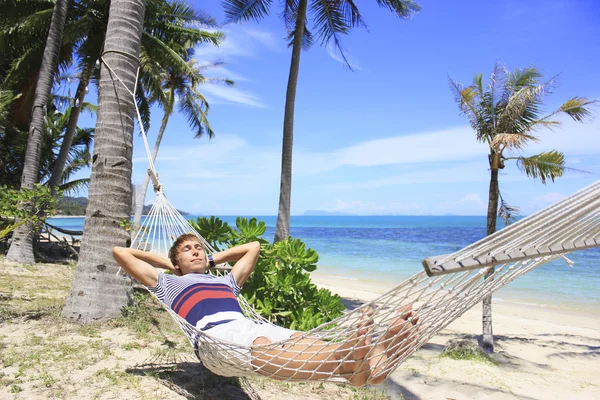 Mann ruht in einer Hängematte unter Palmen am Strand mit weißem Sand und azurblauem Meer — Stockfoto