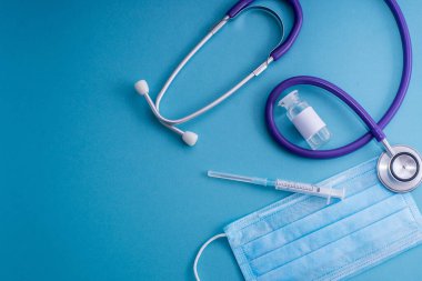 Tıbbi kontrol konsepti. Mavili arka planda en iyi tıbbi ekipman. Düz cerrahi maske, steteskop, haplar, şırınga, termometre, eldivenler ve pano. Tıbbi afiş tasarım şablonu.
