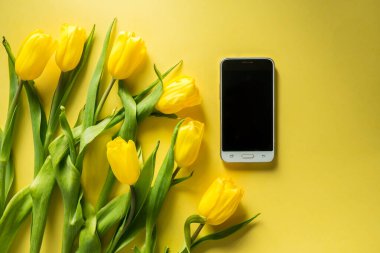 Renkli sarı arka planda, üzerinde bir buket lale olan bilgisayar tableti, panoramik çekim