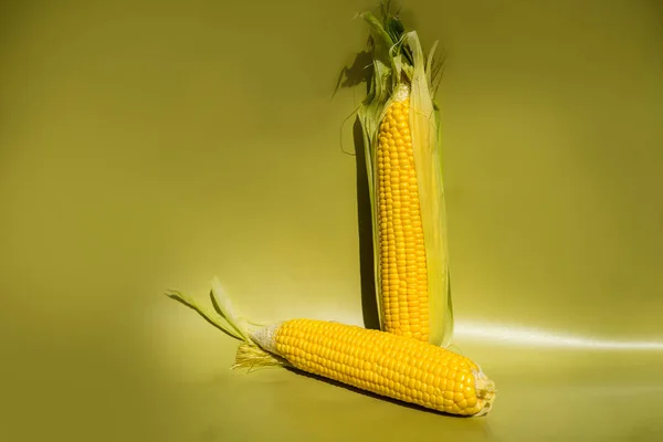 Świeże żółte kolby kukurydzy na zielonym tle. Świeże warzywa. — Zdjęcie stockowe
