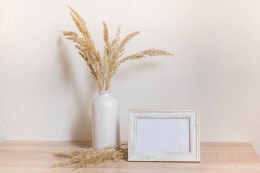 Portre çerçevesi ahşap masada kurumuş çiçeklerle süslenir.