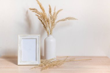 Portre çerçevesi ahşap masada kurumuş çiçeklerle süslenir.