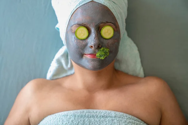 Jovem com máscara cosmética e legumes naturais no rosto. — Fotografia de Stock