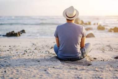 Genç bir adam kumsalda oturmuş gün batımında ufka dik dik bakıyordu.