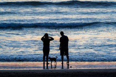Gün batımında sahilde yürüyen genç Latin çiftin silueti.