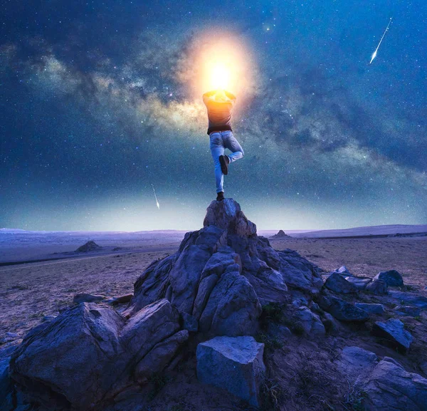 Silhouette of a person in yoga tree position on a rock with Milky Way and shooting stars background