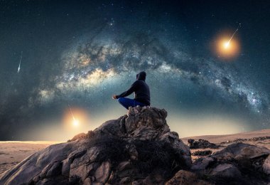 Gece vakti Samanyolu kemerinin altında meditasyon yapan ve kayan yıldızlar