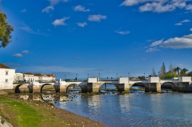 Portekiz 'in Algarve kentindeki Tavira kentindeki Gilao nehri üzerindeki eski Roma köprüsü. Nehrin güzel bir manzarası, nehir kenarındaki görkemli eski binalar ve palmiye kenarlı nehir kıyıları sunar..