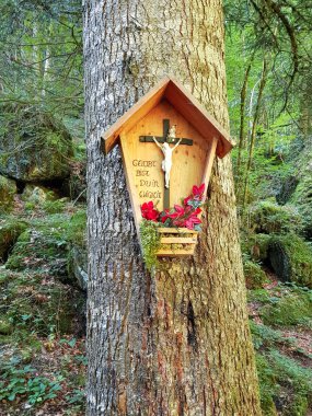 Avusturya, Vorarlberg yakınlarındaki ormandaki büyük bir sandığa bağlı haçlı ve çiçek sunan küçük ahşap bir türbe. Almanca metin, sonsuza dek övgü demek..
