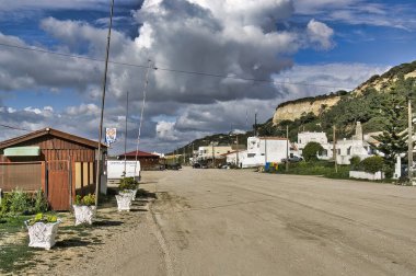 Asfaltsız bir yol boyunca uzanan barlı ve abur cuburlu küçük balıkçı mahallesi dramatik uçurumlar ve bulutlarla dolu bir gökyüzüne karşı. Fonte da Telha, Costa da Caparica, Portekiz.