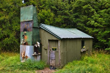 Yoğun bir ormandaki, hayvan kafataslarıyla süslenmiş, öne çıkan bacası olan, taşralı demirden bir kulübe. Gabriel Hut, Sumner Gölü Orman Parkı, Kuzey Canterbury, Güney Adası, Yeni Zelanda