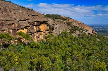 Kuzey Grampians, Victoria, Avustralya 'daki Stapylton Dağı' nda aşınmış kayalar ve yoğun okaliptüs ormanı. Arka planda tarım düzlükleri var. Uçsuz bucaksız kayalıklar yemyeşil okaliptüs ormanları ve mavi gökyüzünün altındaki uzak ovalarla