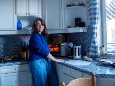 Büyüleyici bir mutfakta tezgahın yanında duran bir kadın yemek hazırlıklarına odaklanıyor. Mikrodalganın yumuşak ışığı, çeşitli mutfak eşyaları ve dekorasyonları arasında onun özelliklerini ön plana çıkarıyor..