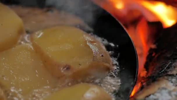 Frying potatoes in butter using a carbon steel frying pan directly on a open camp fire — Stock Video