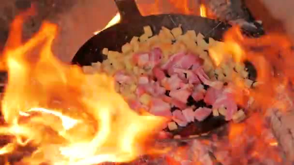 Frying bacon and potatoes over campfire using a carbon steel frying pan — Stock Video