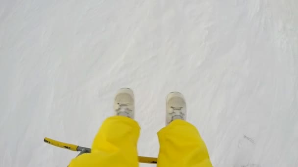 Mädchen in gelben Hosen ruckelt an den Beinen und fährt mit dem Skilift auf den Gipfel der Berge — Stockvideo