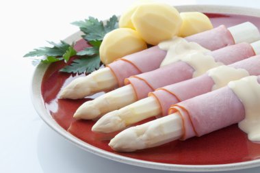 Kuşkonmaz, patates, jambon ve plaka beyaz zemin üzerine maydanoz
