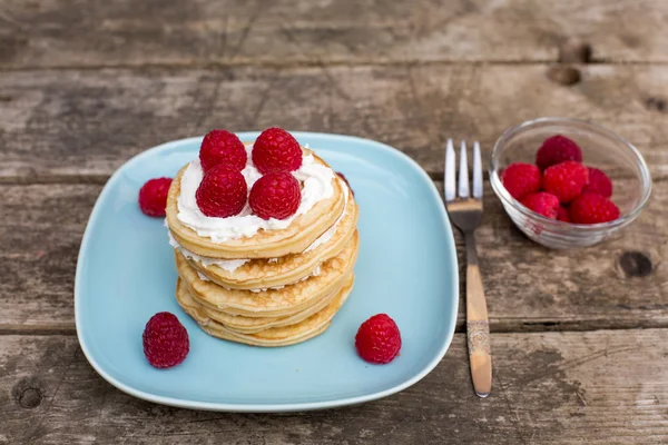 Pancakes with raspberries and cream on blue plate — Stock Photo, Image