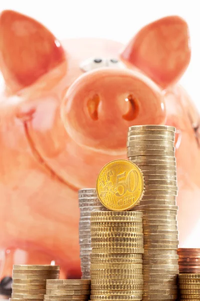 Piggy bank with piles of euro coins on white background — Stock Photo, Image