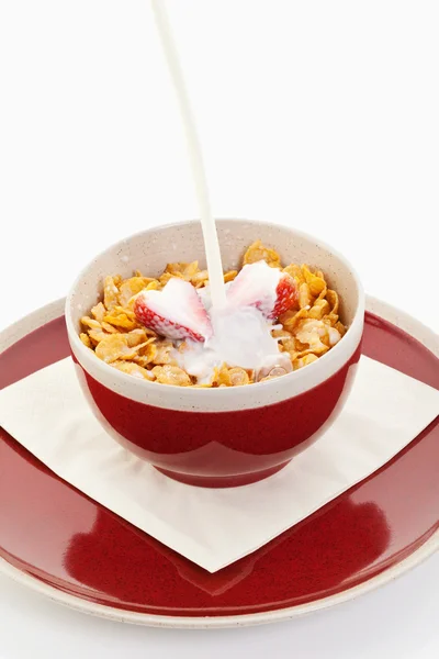 Leite caindo em flocos de milho com morango em tigela vermelha na placa — Fotografia de Stock