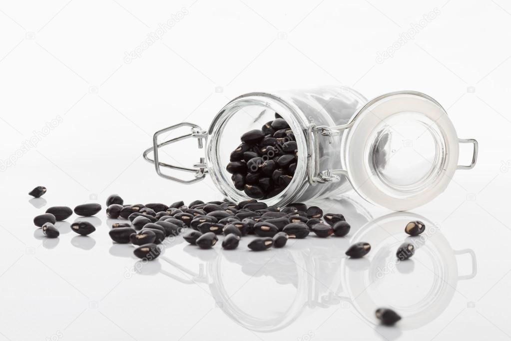 Dry black beans in glass jar spilling on white background