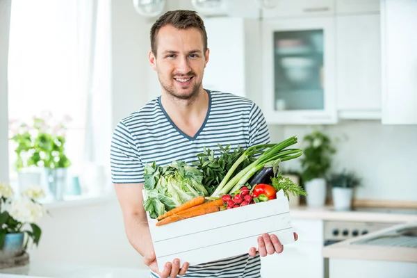 Ung mand med vegetabilsk kasse i køkken - Stock-foto