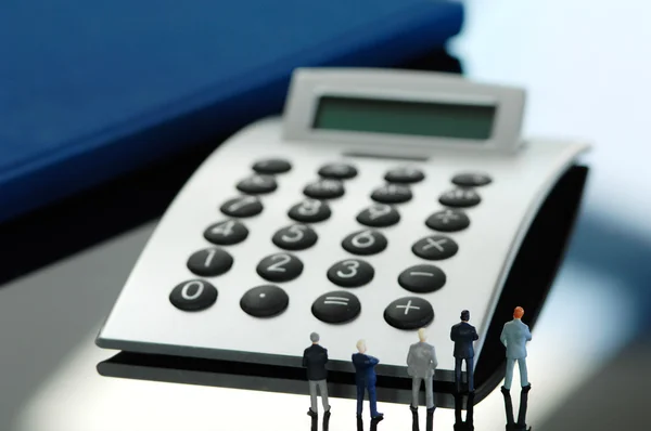 Business men figurines standing in front of calculator, rear vie — Stock Photo, Image